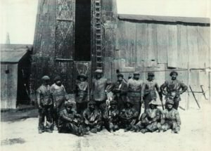 Operarios y jefe frente a torre de petróleo.