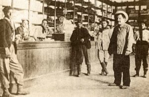 Almacén La Zulemita, de la Familia Zingoni, ubicado en Catan Lil. Detás del mostrador: Roque Muglia y Marcelo Bagli. Apoyado en el mostrador: Nicasio Huarte. Centro: Paulino Abella y otros parroquianos.
