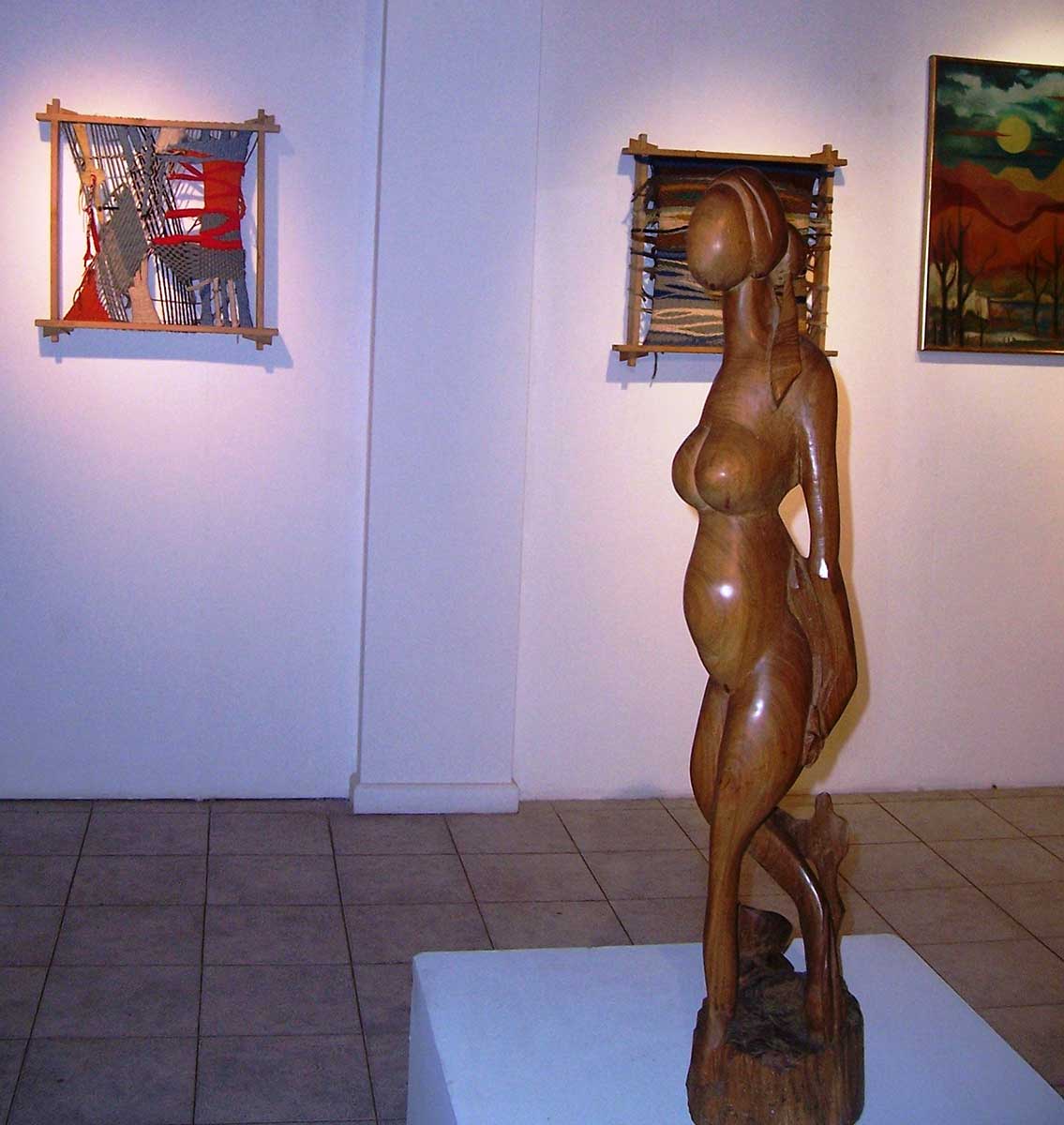 Escultura en madera y tapices detrás, en la exposición retrospectiva realizada en San Martín de los Andes en 2013.